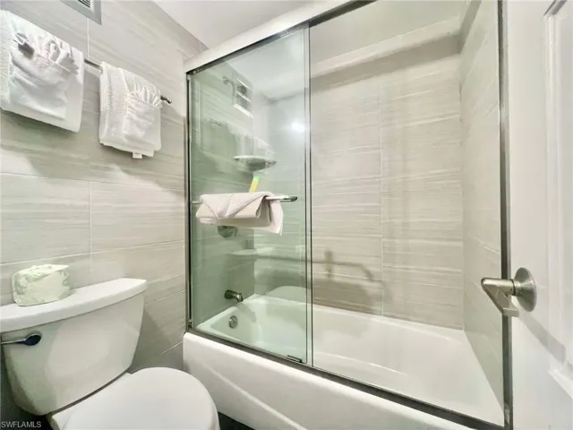 Bathroom with toilet, enclosed tub / shower combo, and tile walls