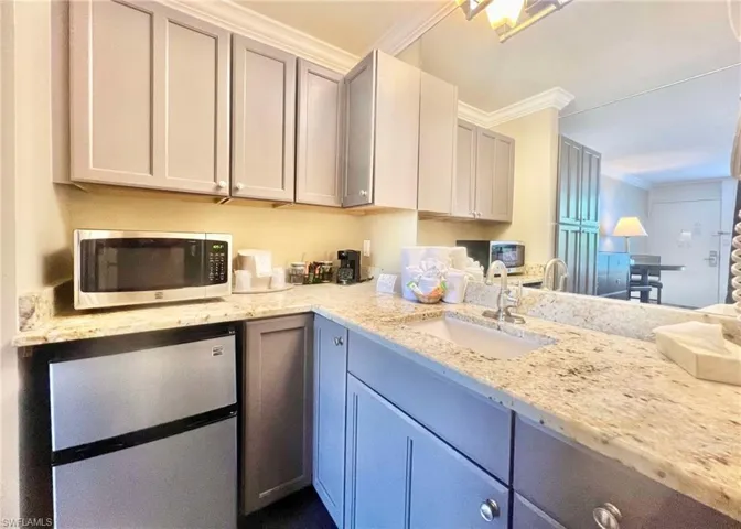 Kitchen featuring gray cabinets, ornamental molding, sink, light stone countertops, and refrigerator