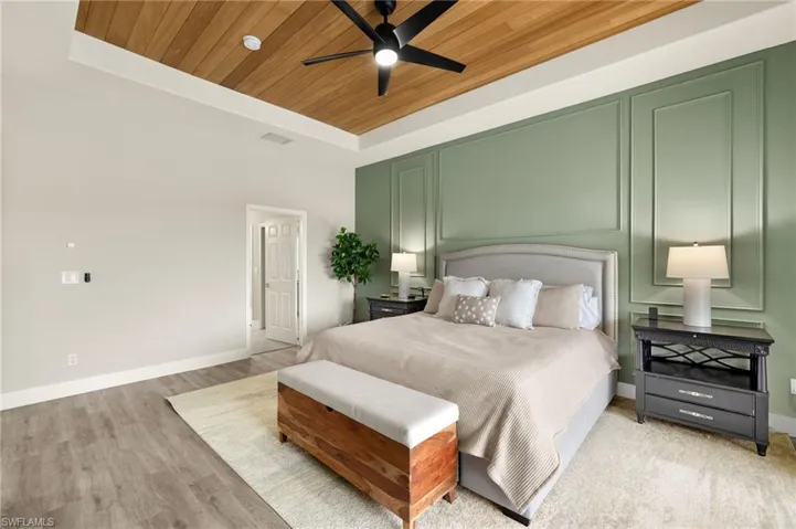Bedroom featuring wooden ceiling, light wood-style flooring, a decorative wall, baseboards, and a raised ceiling.