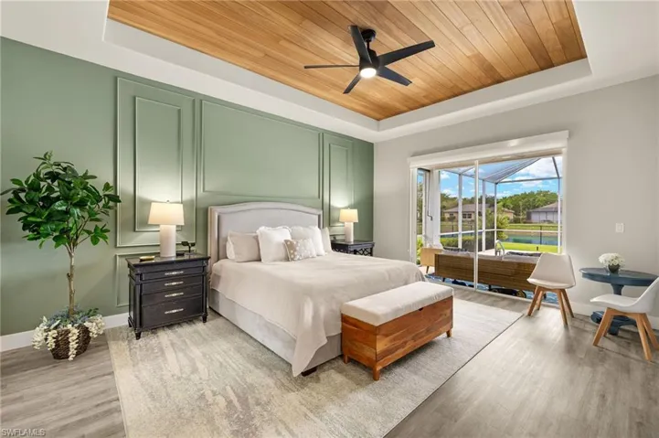 Bedroom featuring wooden ceiling, a ceiling fan, baseboards, a tray ceiling, and light wood finished floors with artistic accent wall.