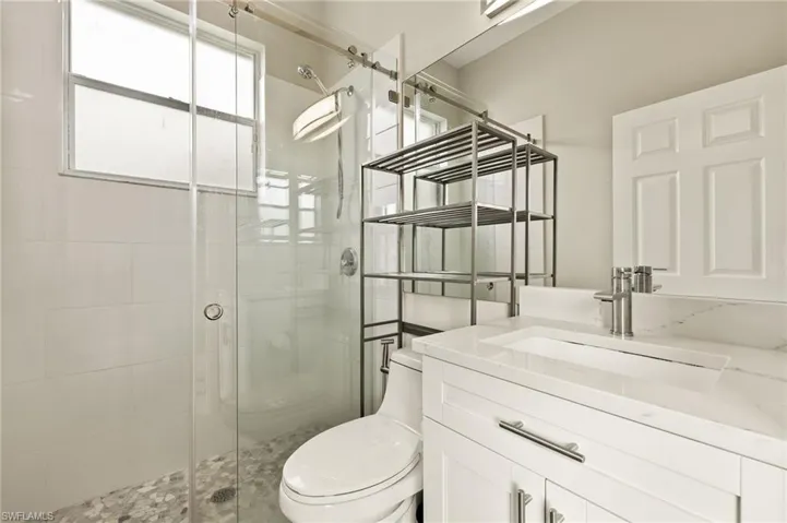 Bathroom featuring toilet, a stall shower, and vanity. Connects to outside pool.