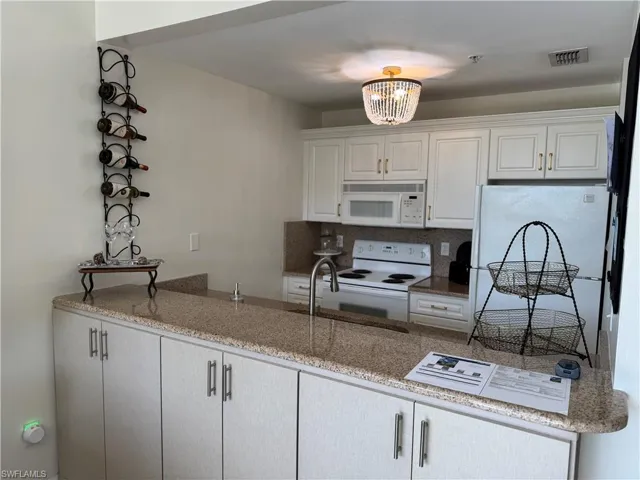 Kitchen featuring white appliances, light stone countertops, white cabinetry, decorative backsplash, and sink