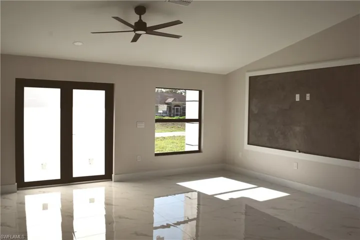 Unfurnished room with marble look tiles, lofted ceiling, baseboards, and a ceiling fan