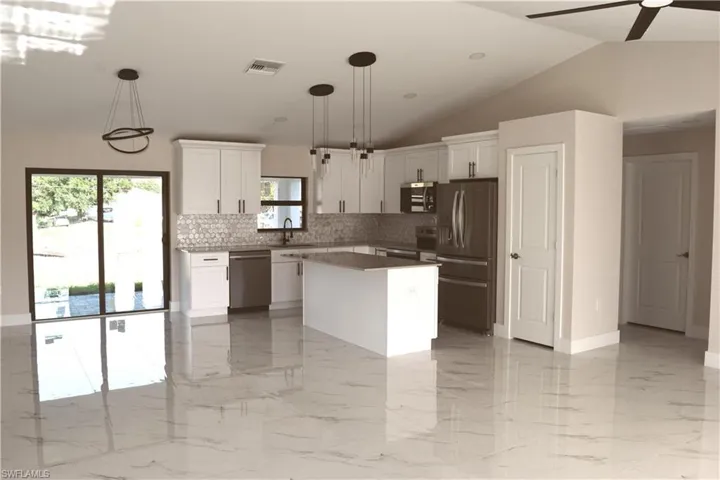 Kitchen featuring stainless steel appliances, a sink, tasteful backsplash, white cabinetry, and a kitchen island
