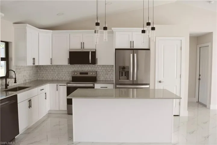 Kitchen featuring appliances with stainless steel finishes, a sink, lofted ceiling, light marble finish floors, and white cabinetry