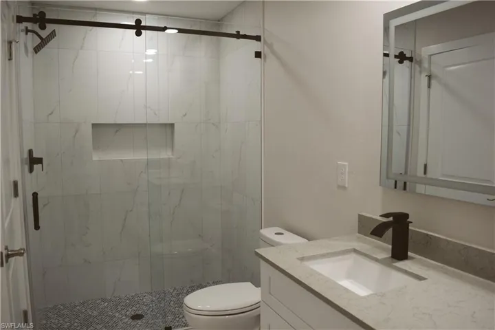 Bathroom with toilet, vanity, and a marble finish shower