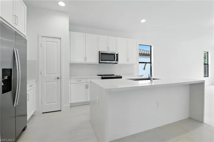 Kitchen featuring stainless steel appliances, white cabinetry, light countertops, an island with sink, and recessed lighting