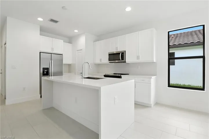 Kitchen featuring stainless steel appliances, white cabinetry, a kitchen island with sink, light countertops, and recessed lighting