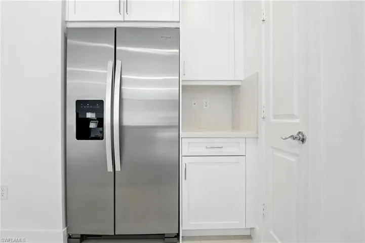 Kitchen with stainless steel fridge, white cabinetry, and light countertops