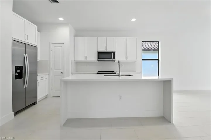 Kitchen featuring stainless steel appliances, light countertops, white cabinets, a kitchen island with sink, and recessed lighting