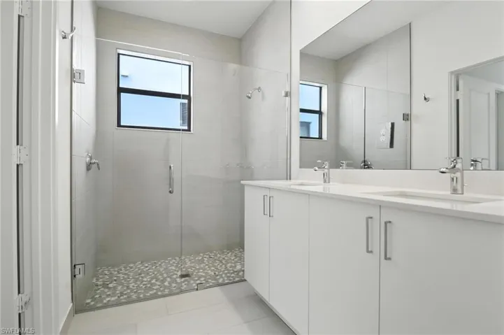 Full bathroom featuring a shower stall, double vanity, plenty of natural light, and tile patterned flooring