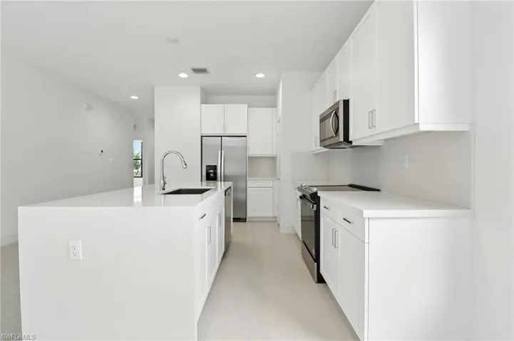 Kitchen featuring appliances with stainless steel finishes, recessed lighting, a kitchen island with sink, white cabinets, and light countertops