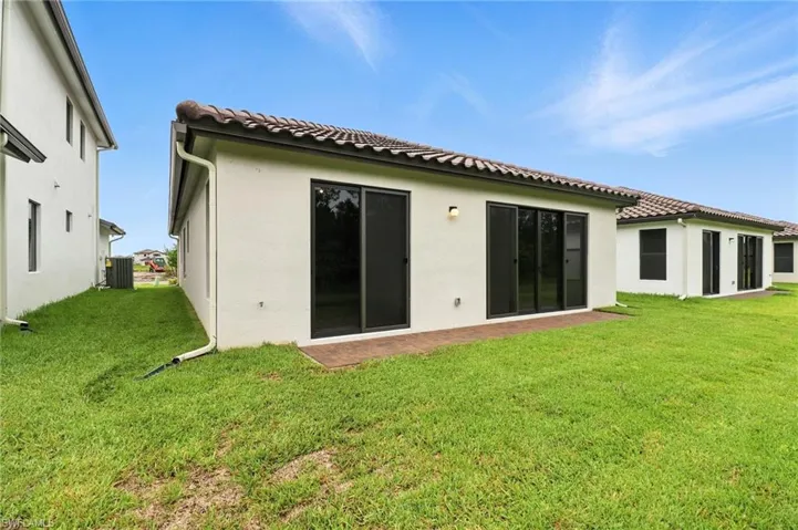 Back of house with a yard, stucco siding, and a tiled roof
