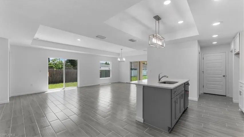 Dual tone kitchen featuring a raised ceiling, wood tiled floors, an island with sink, open floor plan, and light stone countertops