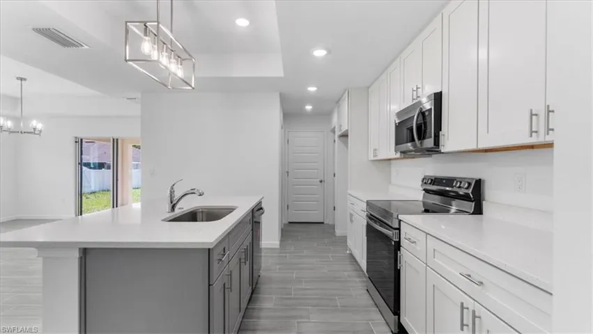 Kitchen featuring stainless steel appliances, dual tone cabinetry, a chandelier, light stone counters, and an island with sink