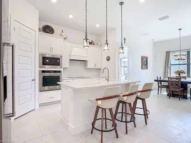 Kitchen with decorative light fixtures, built in appliances, an island with sink, a kitchen breakfast bar, and white cabinets