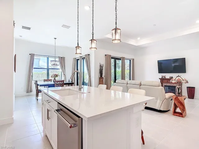 Kitchen with white cabinets, pendant lighting, stainless steel dishwasher, light stone counters, and open floor plan