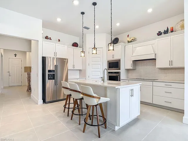 Kitchen with appliances with stainless steel finishes, pendant lighting, an island with sink, a breakfast bar, and white cabinetry