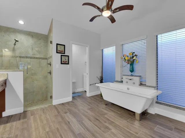 Bathroom with a shower stall, a freestanding tub, a ceiling fan, and wood finish floors
