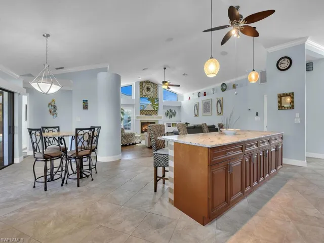 Kitchen featuring ornamental molding, open floor plan, ceiling fan, a kitchen breakfast bar, and a lit fireplace