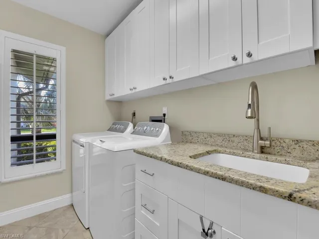 Laundry area featuring light tile patterned floors, baseboards, separate washer and dryer, a sink, and cabinet space