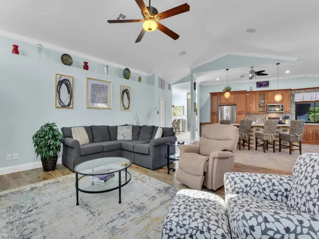 Living room with visible vents, vaulted ceiling, ornamental molding, and ceiling fan