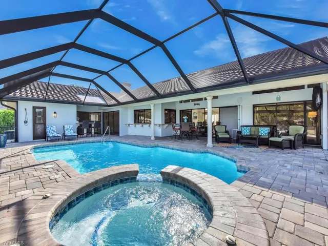 View of swimming pool featuring a patio area, a pool with connected hot tub, an outdoor living space, outdoor dry bar, and a lanai