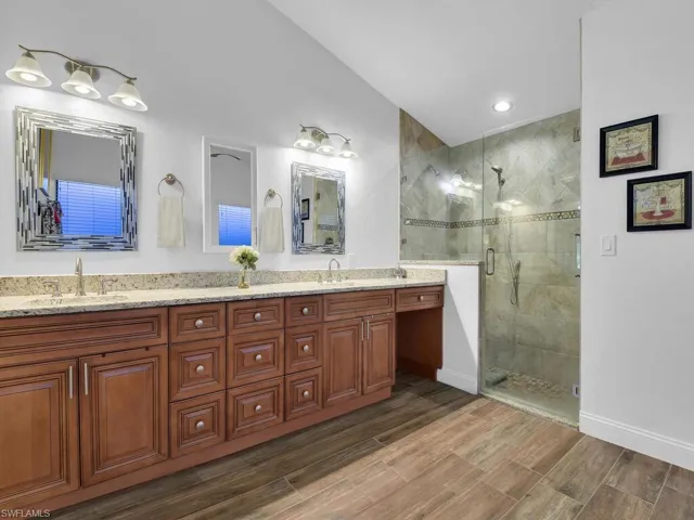 Full bath with wood finished floors, a sink, a stall shower, and lofted ceiling