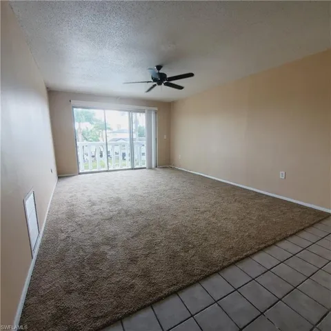 Carpeted spare room with a textured ceiling, tile patterned flooring, and a ceiling fan