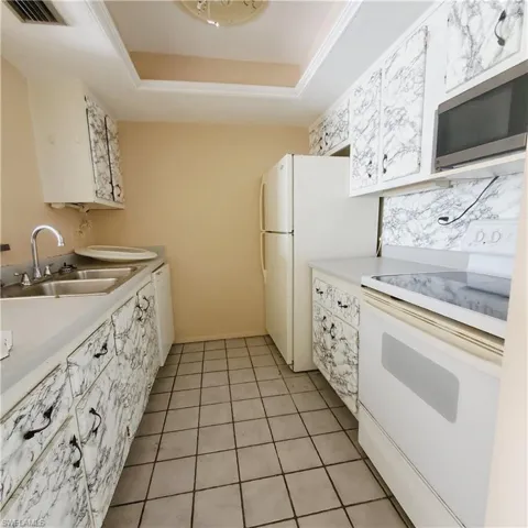 Kitchen with white appliances, light countertops, a tray ceiling, light tile patterned flooring, and white cabinetry