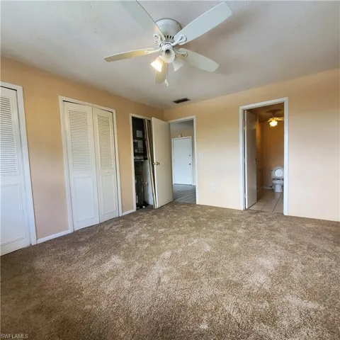 Unfurnished bedroom featuring connected bathroom, two closets, carpet floors, and ceiling fan