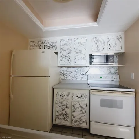Kitchen featuring white appliances, light tile patterned floors, a tray ceiling, and light countertops