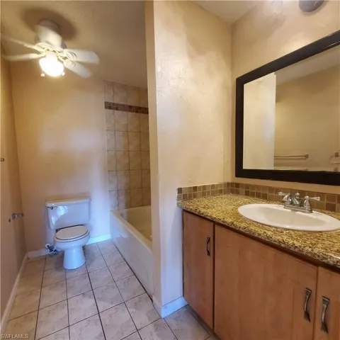 Full bathroom featuring vanity, light tile patterned flooring, ceiling fan, a textured wall, and washtub / shower combination