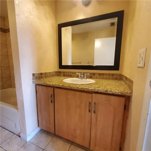 Full bath featuring a textured wall, vanity, light tile patterned floors, and tasteful backsplash
