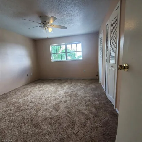 Unfurnished bedroom with multiple closets, a textured ceiling, carpet flooring, and ceiling fan