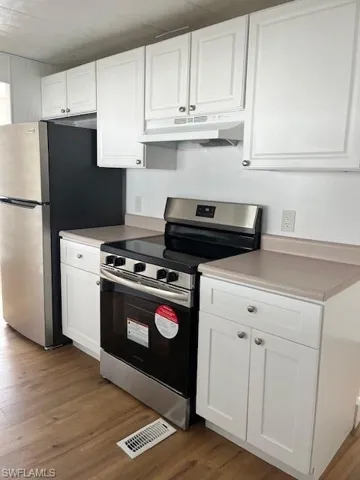 Kitchen featuring white cabinetry, hardwood / wood-style floors, extractor fan, and stainless steel range oven