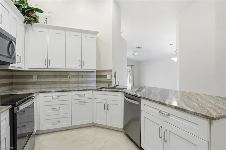 Kitchen with light stone counters, appliances with stainless steel finishes, white cabinetry, backsplash, and a peninsula