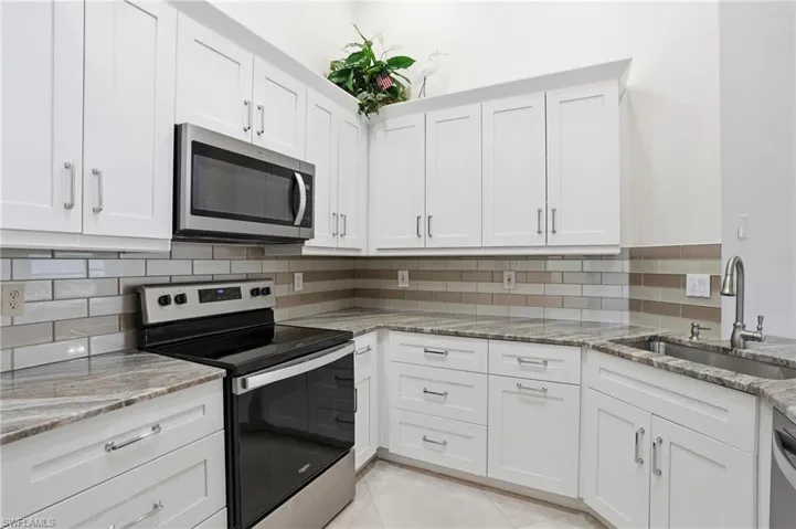 Kitchen with stainless steel appliances, white cabinetry, light stone counters, and decorative backsplash