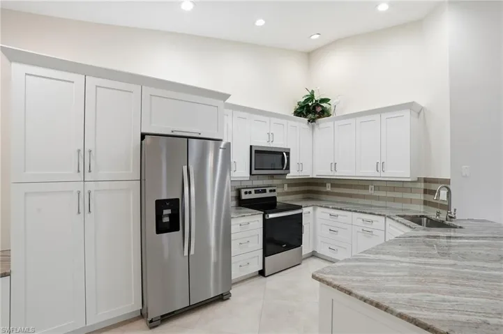Kitchen featuring light stone countertops, appliances with stainless steel finishes, white cabinets, and recessed lighting