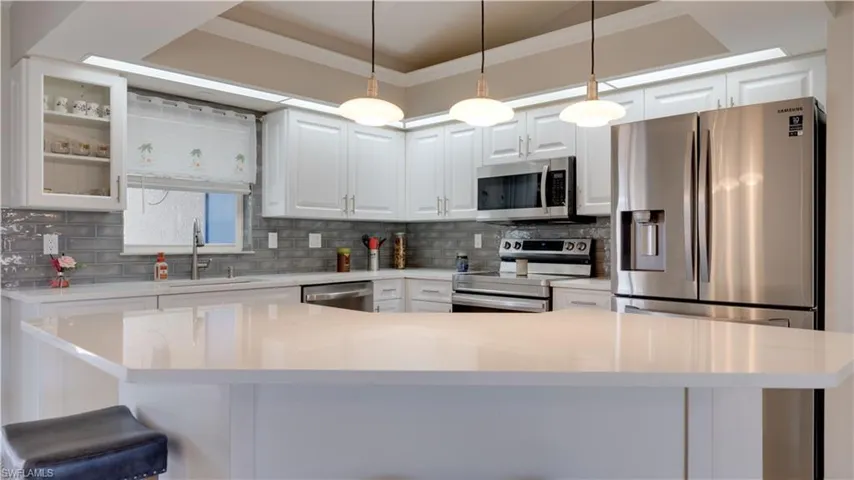 Kitchen with white cabinetry, appliances with stainless steel finishes, ornamental molding, and pendant lighting