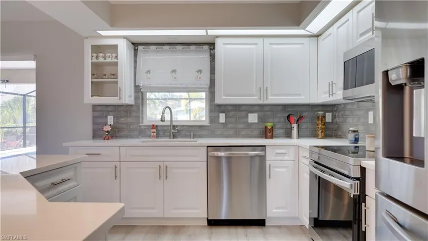 Kitchen with appliances with stainless steel finishes, white cabinets, light stone countertops, and backsplash