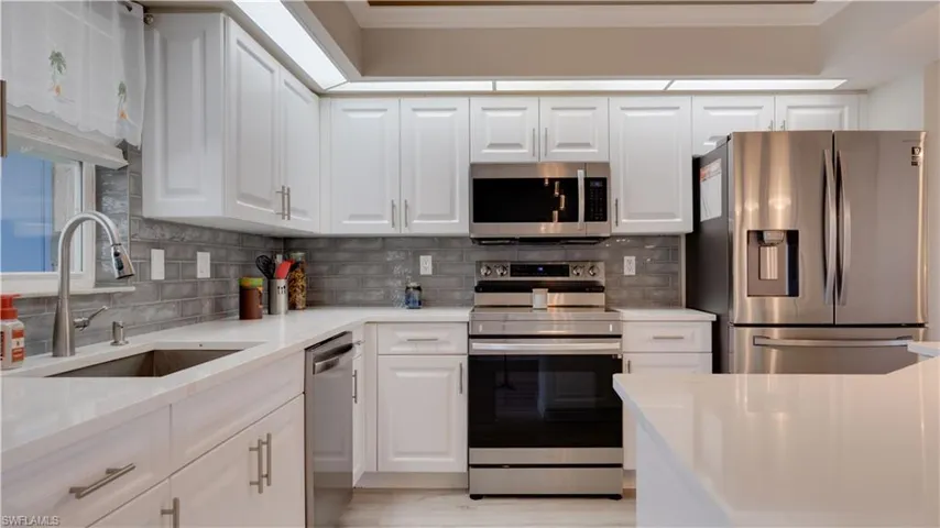 Kitchen with stainless steel appliances, white cabinetry, light stone countertops, ornamental molding, and backsplash