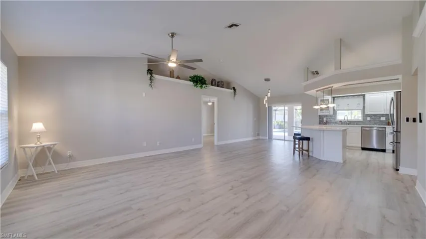 Unfurnished living room with high vaulted ceiling, ceiling fan, light wood-style flooring, and a chandelier