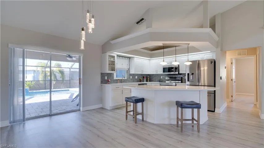 Kitchen featuring white cabinetry, glass insert cabinets, a breakfast bar, pendant lighting, and tasteful backsplash