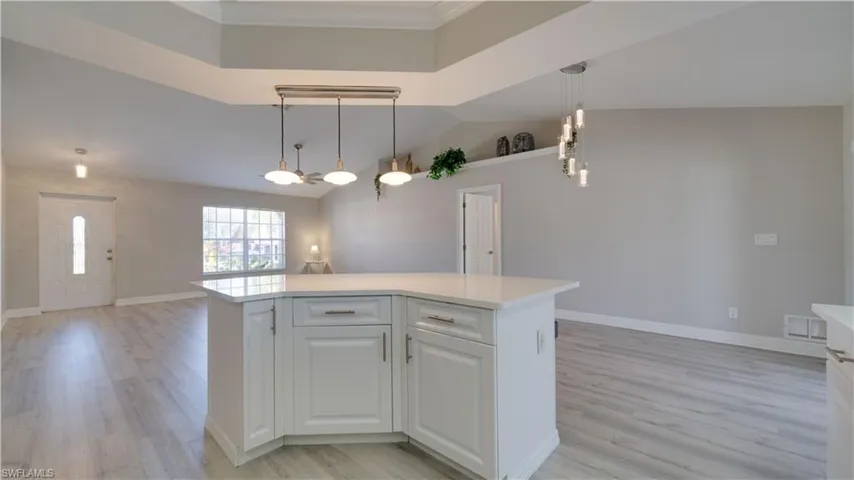 Kitchen with decorative light fixtures, light wood finished floors, white cabinets, a center island, and vaulted ceiling