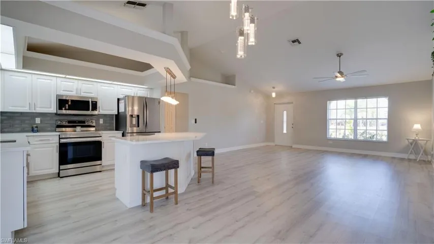 Kitchen with white cabinets, stainless steel appliances, a kitchen breakfast bar, a kitchen island, and hanging light fixtures