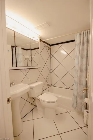 Bathroom featuring shower / bath combo with shower curtain, toilet, tile patterned floors, and tile walls