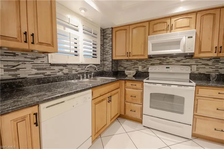 Kitchen with sink, tasteful backsplash, light tile patterned flooring, white appliances, and dark stone countertops