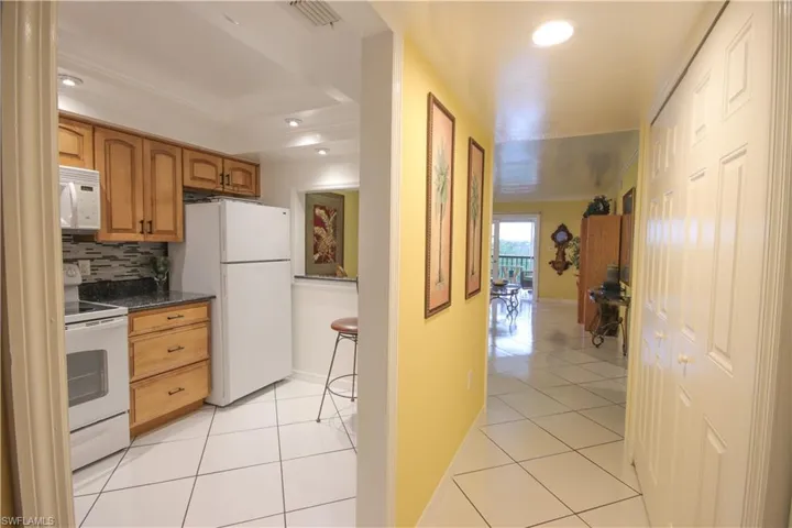 Kitchen featuring dark stone counters, light tile patterned floors, a tray ceiling, white appliances, and decorative backsplash