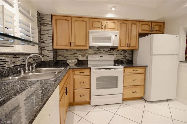 Kitchen with sink, white appliances, light brown cabinetry, and light tile patterned floors